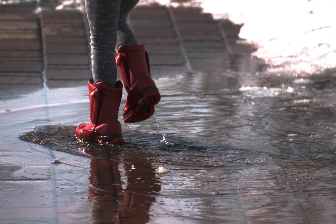 幼い子供が赤いレインブーツを履いて雨水の上を歩いている